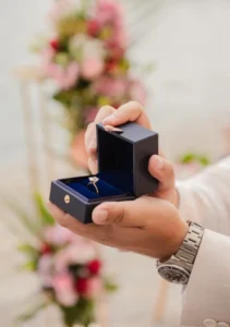 Hand holding ring box with blurry flowers